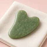 Illustration of a green jade gua sha stone resting on a folded cream towel